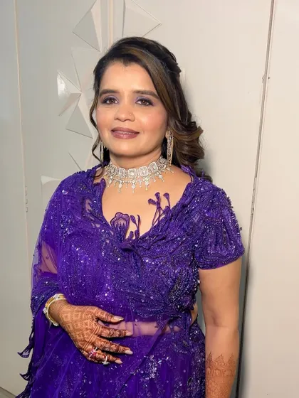 A full-length view of a stunning guest makeup look. The purple sequined saree is complemented by a shimmery purple smokey eye, creating a cohesive and glamorous style.
