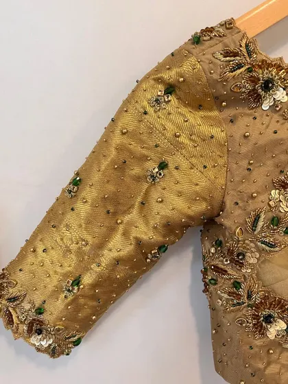 A close-up of the sleeve of the gold bridal blouse, showing the detailed beadwork and sequins that add a touch of color and sparkle.