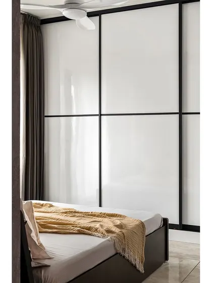 A high-gloss white wardrobe with black metal framing frees up floor space and reflects light, making this compact master bedroom feel more spacious.