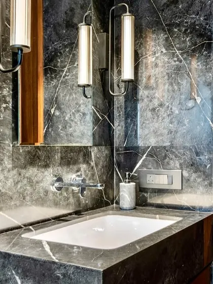 This powder room in the Parishram residence uses a dark, dramatic marble to create a moody and sophisticated atmosphere. Vertical sconce lights add a soft, ambient glow.