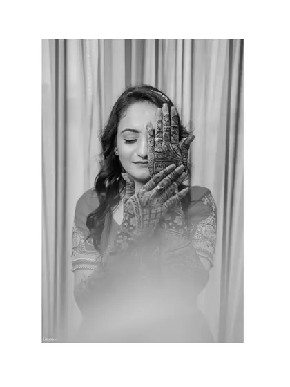 An artistic black and white portrait of Akshara, with her henna-covered hands framing her face. This is a creative and beautiful way to showcase the Mehendi art.