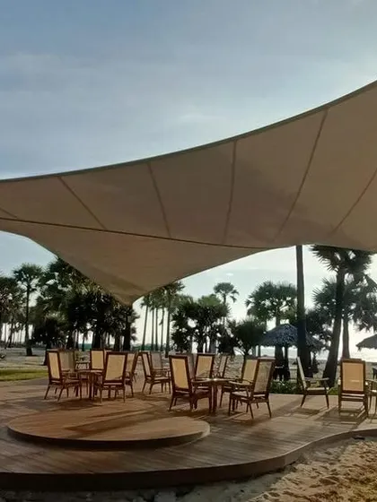 The lightweight tensile structure provides an elegant, shaded seating area on the sand, offering a comfortable spot to enjoy the sea breeze and coastal views.