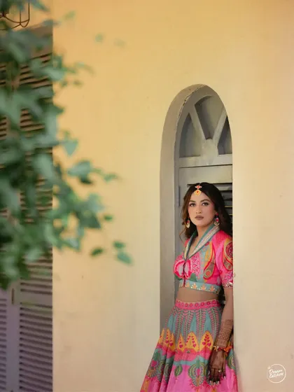 The bride peeking out from an arched window, creating a lovely, framed portrait during her Nashik Haldi.