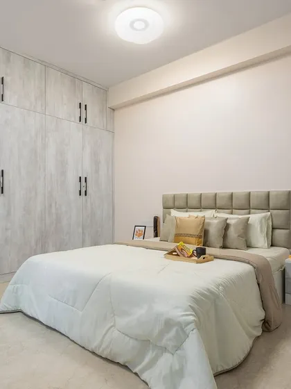 A simple yet elegant bedroom design with a textured, light-wood-finish wardrobe that extends to the ceiling, maximizing storage and creating a sense of height.