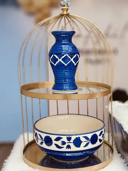 A close-up of the decorative props on a cake table, including a blue ceramic vase inside a golden birdcage, all matching the blue Moroccan theme.