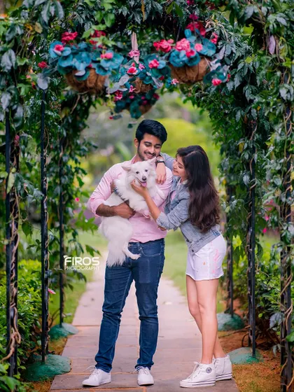 A full-length shot of the couple and their dog under the floral arch. This pose shows their casual, stylish outfits and the happy, relaxed atmosphere of a pet-friendly photoshoot.