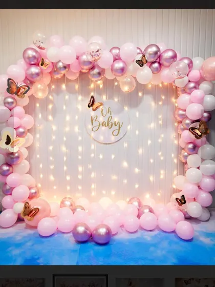 A beautiful 'Oh Baby' photo booth backdrop. A square frame of pink and white balloons is set against a curtain of fairy lights.