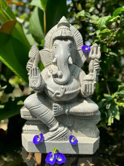 Our Ganappa statue, adorned with butterfly pea flowers, is captured in a lush garden, embodying its role as a remover of obstacles.