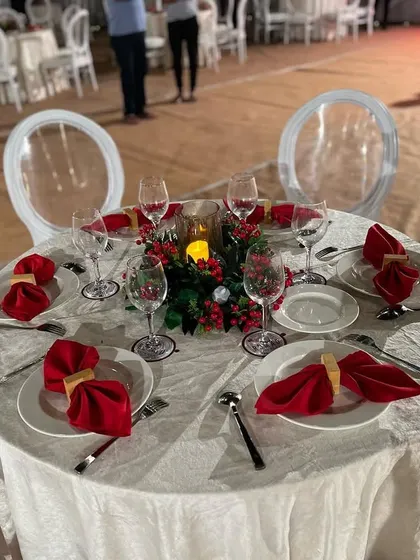 A round table setup for a Christmas event. The crisp white linen, red napkins, and a festive centerpiece with holly and candles create a cheerful and sophisticated holiday look.