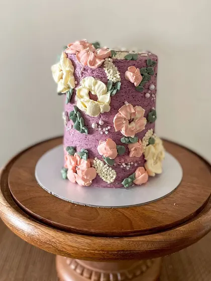 This tall barrel cake is a great example of my floral buttercream work. The textured purple frosting is adorned with hand-piped flowers in pastel pinks and yellows, creating a beautiful garden effect.