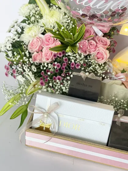 A detailed shot of the 20th birthday hamper, highlighting the fresh pink roses, delicate baby's breath, and the elegantly wrapped gift boxes from brands like Misham and Muse, showing the quality of the curated items inside.