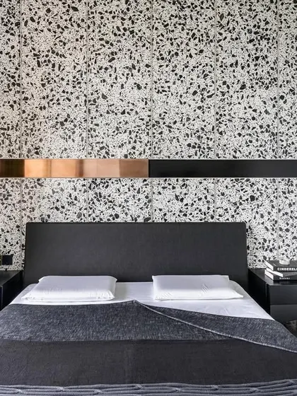 The guest room in 'A Wedged Haus' features a neutral palette of terrazzo and grey stone. The design is punctuated by a copper cuboid wedged into the headboard, creating a sharp, metallic focal point.