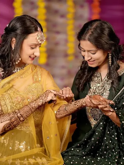 A candid shot of the bride showing her Mehandi to her sister or friend. This image captures a sweet, personal moment between loved ones.