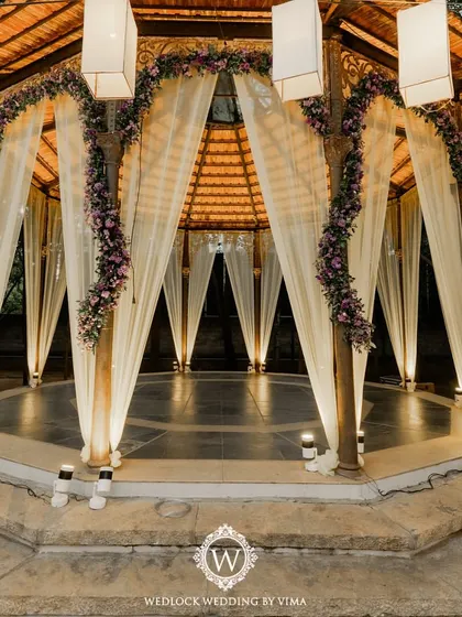 A simple yet elegant reception setup with soft lantern lighting and delicate drapes on the gazebo. The lush purple-themed florals and romantic centerpieces tied the whole look together.