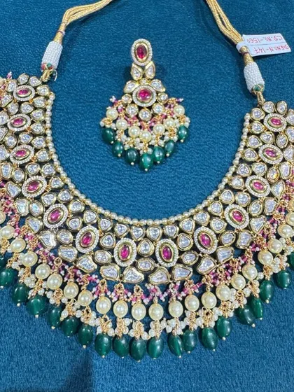 A beautiful bib-style necklace featuring fine kundan work, pearls, and a mix of ruby and emerald colored stones.