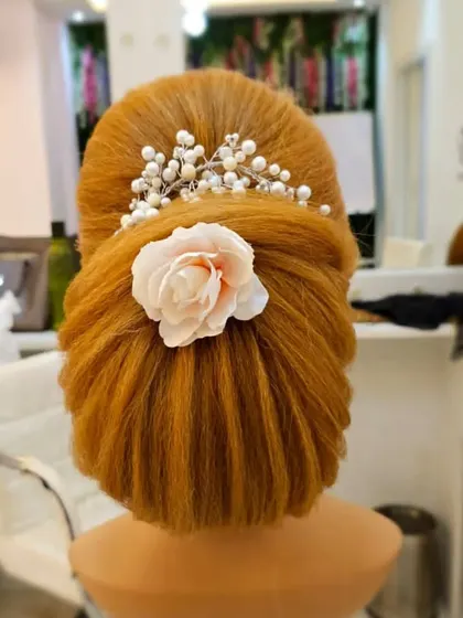 A classic French bun with a modern twist, accessorized with a delicate flower and pearl hairpiece. This is a versatile look for receptions or parties.