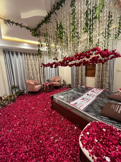 An incredibly romantic room setup with a ceiling decorated with hanging vines and a cloud of red roses over the bed. The entire floor is a carpet of red rose petals.