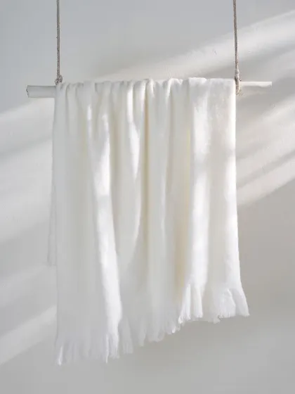 A simple white throw blanket hanging from a wooden rod. The play of light and shadow across the fabric highlights its soft texture and creates a serene, minimalist image.
