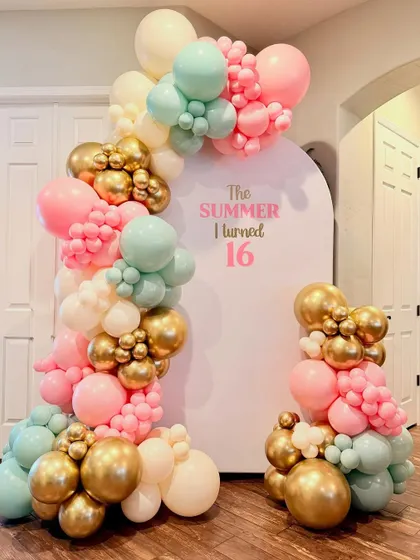 A trendy "The Summer I turned 16" birthday theme. This setup features a modern arched backdrop and an organic balloon garland in a beautiful pastel pink, mint, and gold color scheme.