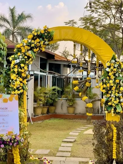 The entrance to an outdoor haldi ceremony, marked by a bright yellow arch decorated with yellow and white flowers. A welcome sign announces the event, setting a cheerful tone right from the start.