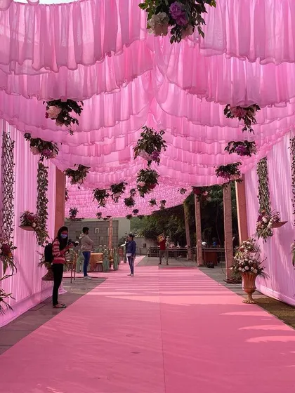 The entrance walkway for a daytime event, decorated with a ceiling of pink drapes and hanging floral arrangements, creating an immersive and colorful welcome for guests.