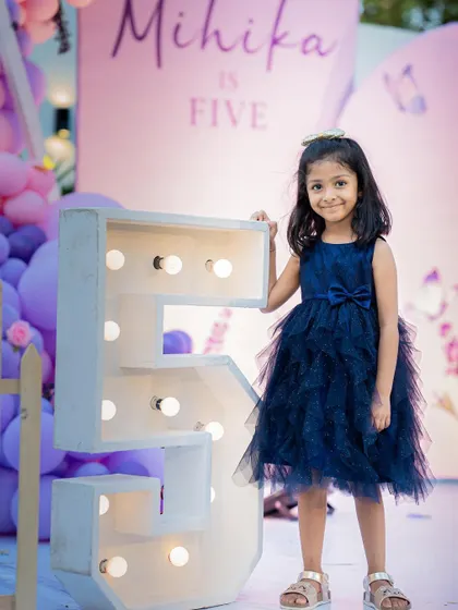 The birthday girl proudly standing next to her illuminated number "5" at her party.