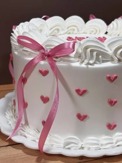 Every little detail counts. This close-up shows the delicate pink hearts and ribbon on a classic white buttercream cake, proving that simple designs can be incredibly sweet and charming.