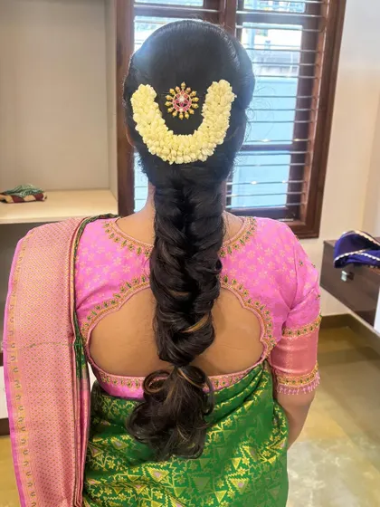 A fishtail braid adorned with a U-shaped jasmine gajra and a central pink stone accessory.