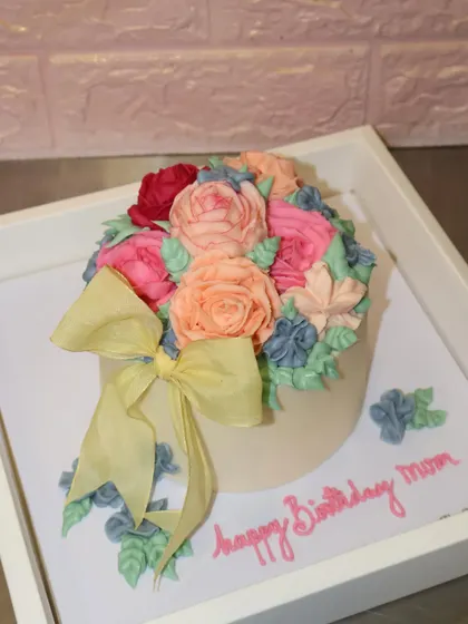 A cake that looks like a beautiful bouquet of flowers. This stunning creation features a variety of hand-piped buttercream flowers and is finished with a delicate yellow bow.