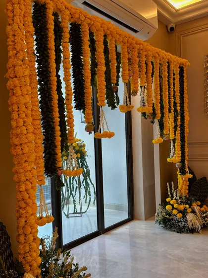 A full view of the marigold and mango leaf toran framing a doorway. This is a classic decoration for auspicious occasions, symbolizing prosperity and good fortune.