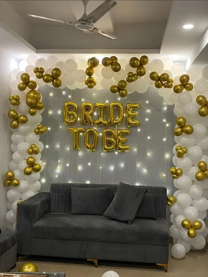An elegant 'Bride to Be' photo corner. I created a backdrop of white and gold balloons with a curtain of fairy lights, providing a perfect spot for photos with a comfortable sofa.