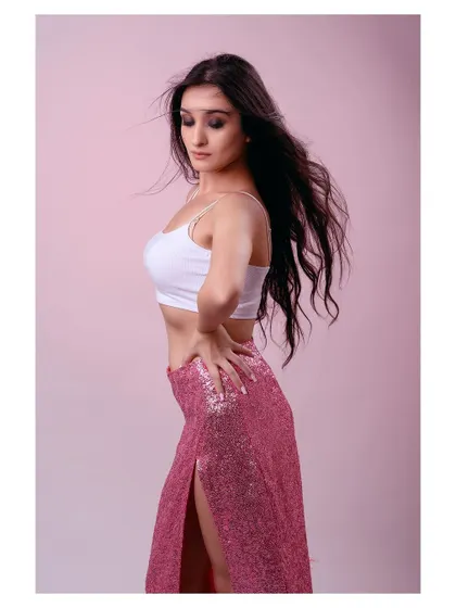 A soft and feminine portrait against a pink studio background. The flowing hair and sequined skirt create a glamorous and dreamy atmosphere.