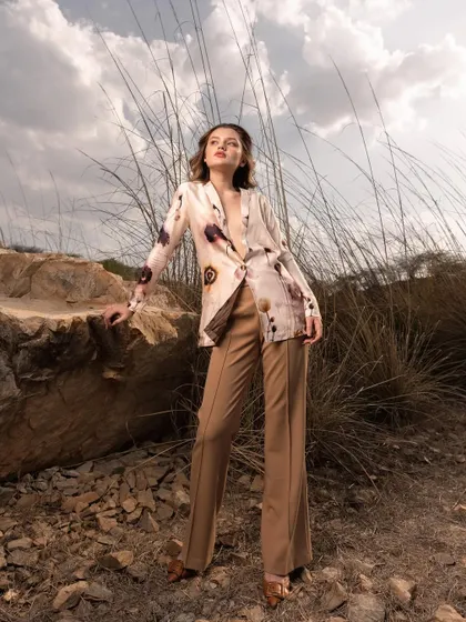 A wide shot that places the model and her outfit within the expansive landscape. The dramatic sky and earthy tones complement the printed blazer and flared trousers, creating a high-impact campaign image.