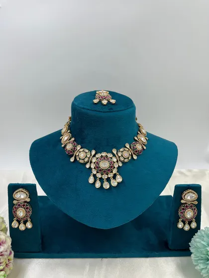 A pair of Moissanite Kundan earrings with a circular design. The ruby-colored stones and white stone drops make these a vibrant and attractive choice.