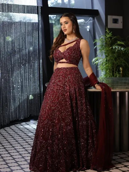 A full-length shot of the bride in her magnificent maroon sequin lehenga. The makeup is glamorous yet sophisticated, perfect for a cocktail night.