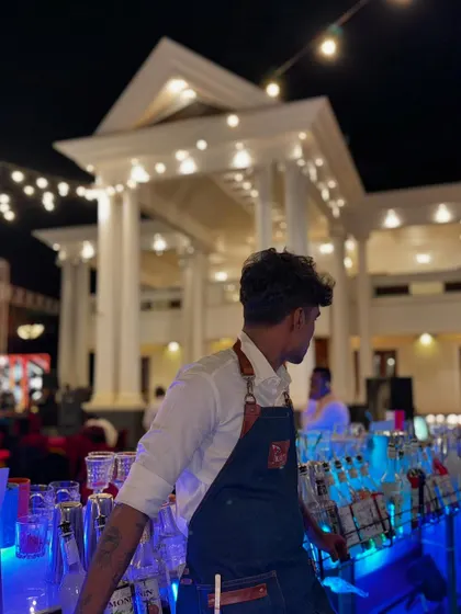 A bartender at his station, focused and ready for the night ahead, with the impressive venue behind him.