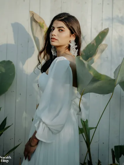 A portrait of serene beauty. The bride, dressed in a flowing white dress, looks directly at the camera, framed by lush green leaves that add a touch of natural elegance.