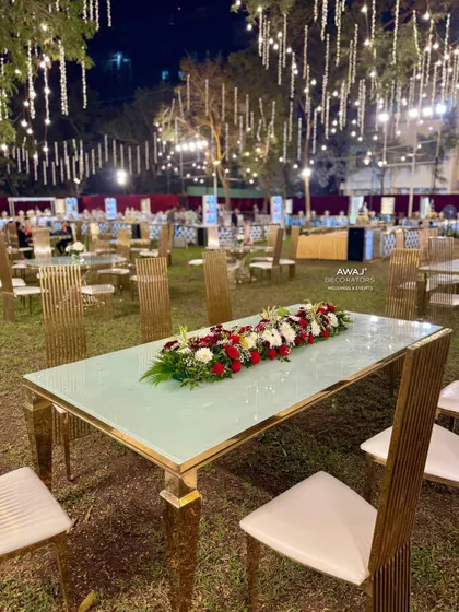 A modern, gold-trimmed dining table with a long floral runner, set against the backdrop of a beautifully lit event space.