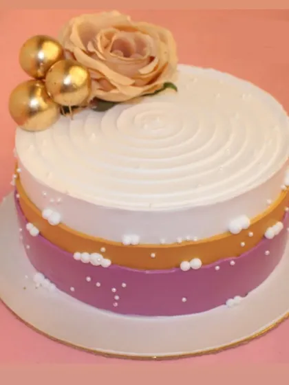 An elegant cake with purple and gold bands, topped with a delicate rose and golden spheres.