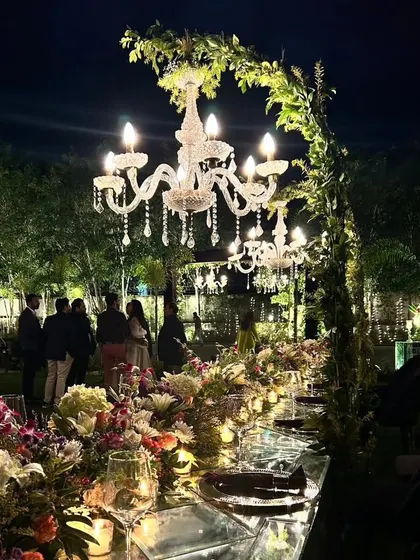 A long, mirrored dining table reflects the enchanting chandeliers above. The table is adorned with a continuous runner of exotic flowers for a truly opulent look.