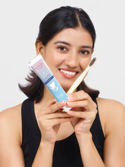A clean and friendly product shot for an oral care brand. The model holds the toothpaste and toothbrush with a bright smile, creating a trustworthy and effective visual for e-commerce.
