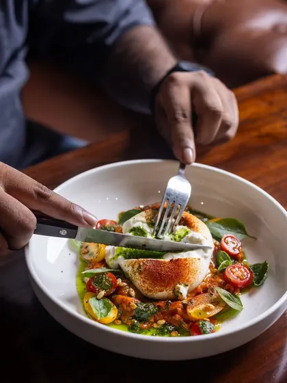 A customer digs into the Burrata Salad, cutting into the creamy cheese. It's a satisfying and interactive dining experience.