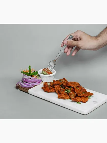 A hand is shown dipping a piece of the chicken appetizer into the chutney. This action shot makes the food feel more immediate and interactive for the online viewer.