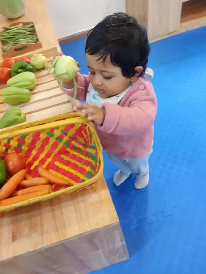 A toddler explores a basket of fresh vegetables, learning their names, colors, and textures in a hands-on way.