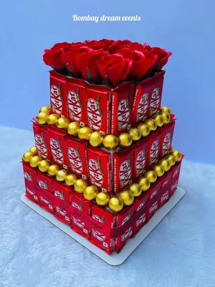 A classic three-tiered KitKat tower, accented with gold-wrapped chocolates and topped with red roses. This makes for a perfect gift or a delightful addition to your dessert table.