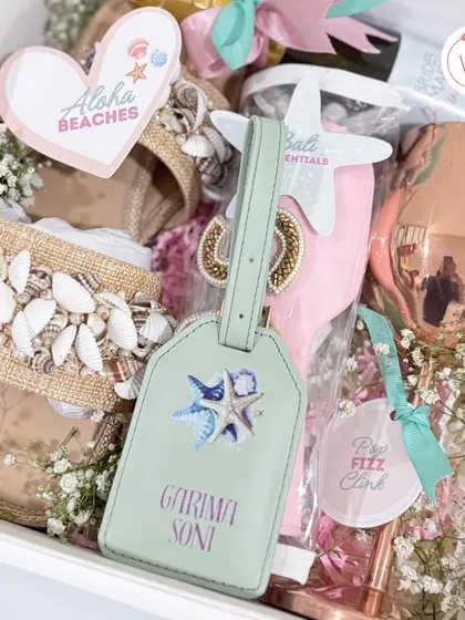 A closer look inside the Bali-themed bridesmaid hamper, showing a personalized luggage tag, a rose-gold wine glass, and other travel essentials.