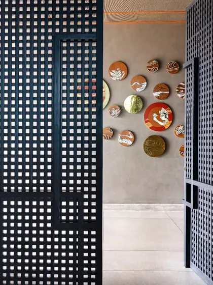 A view through a custom perforated blue door at Anthea Pharma, leading to the guest lounge. A bold artwork crafted from wood, paint, and brass offers a visual preview of the space ahead.
