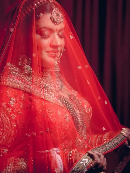 A graceful portrait of a bride holding her red veil, captured in a moment of quiet contemplation.