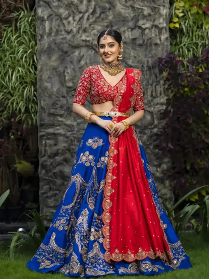 This raw silk lehenga plays with a bold and beautiful combination of royal blue and vibrant red. The skirt is adorned with exquisite gold zardosi details, creating a look that is undeniably regal and perfect for a grand wedding.