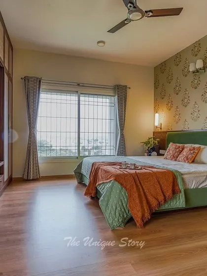 A wide view of the renovated master bedroom, showing the new custom wardrobes with an integrated TV unit. The floral wallpaper and green bed create a cohesive and elegant design with a nod to Indian heritage.